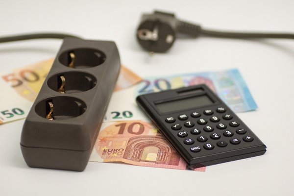 Symbolfoto mit Mehrfachsteckdose, Taschenrechner und Geldscheinen